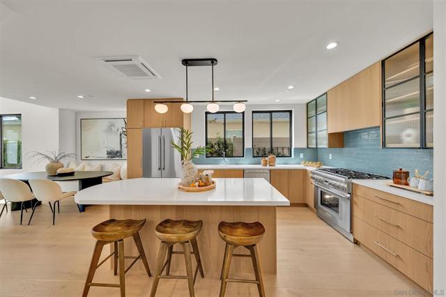 Bright kitchen with a long island, three stools, pendant lights and wood cabinets